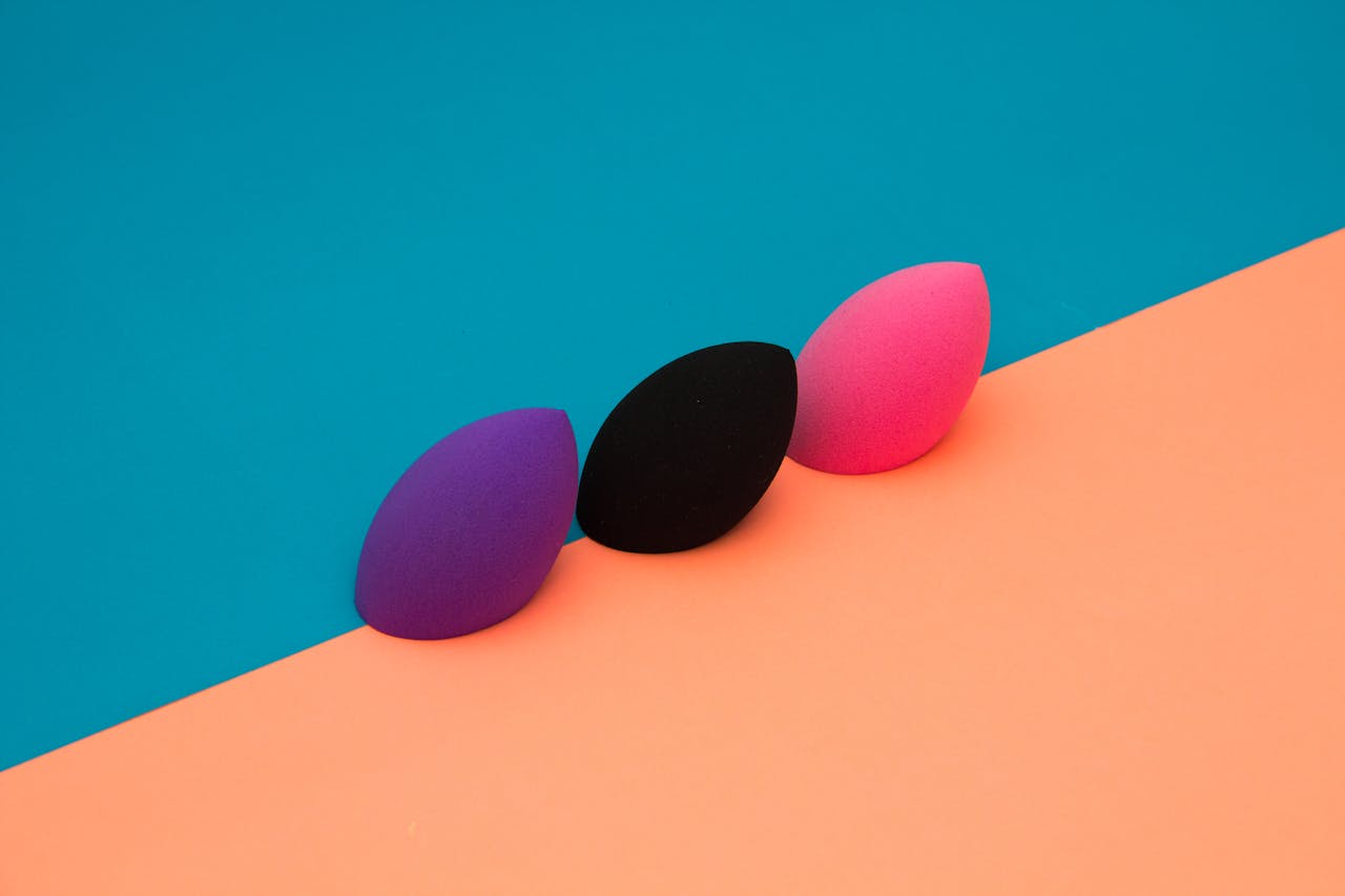 Three makeup sponges on a vibrant, split-color background create a striking minimalist composition.